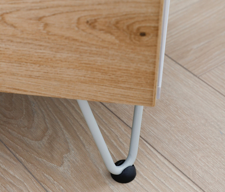 Detail einer Ecke der Rauch Kommode »Homey« mit Holzmaserung und weißen Beinen auf einem Holzboden.