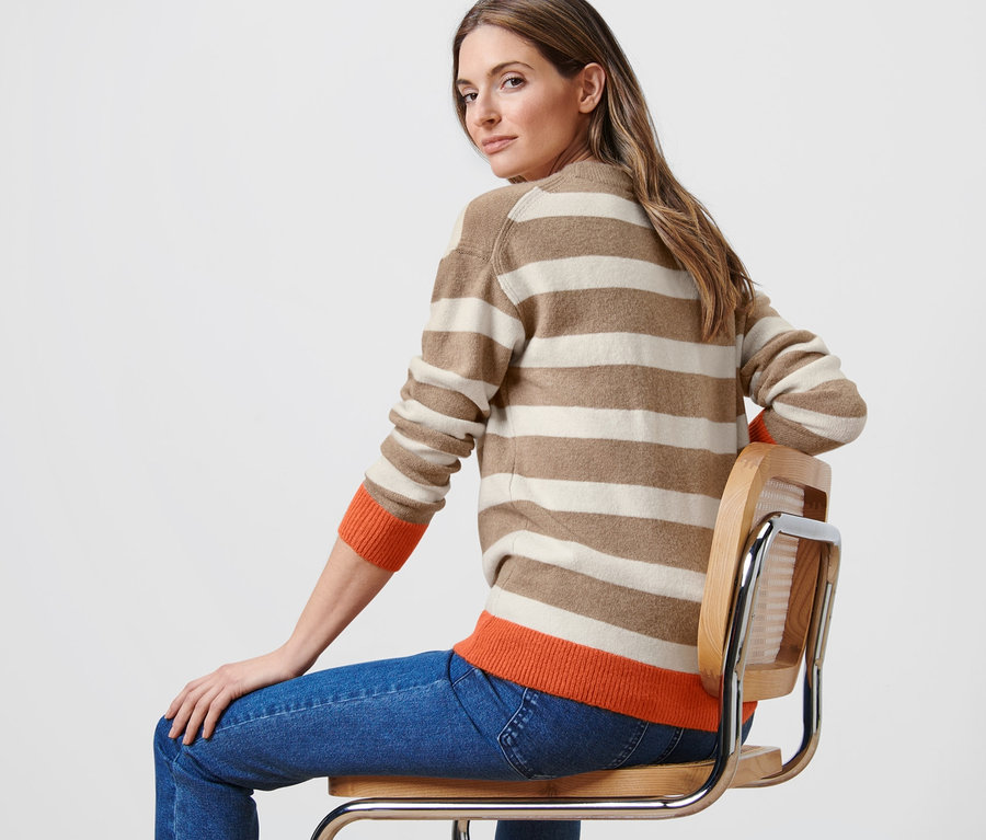 Frau sitzt auf Stuhl und trägt gestreiften Strickpullover.