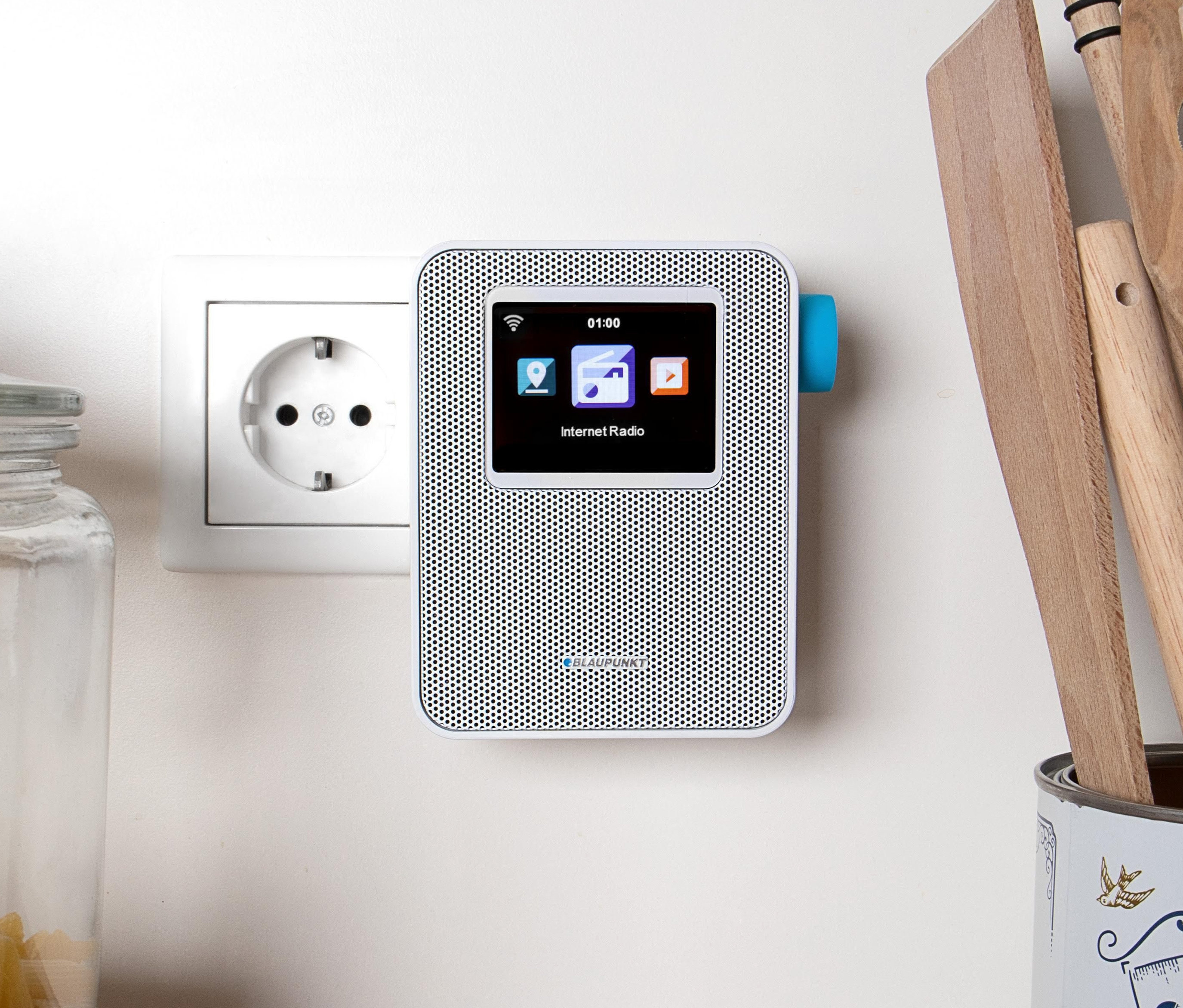 Ein weißes Blaupunkt Internet-Steckdosen-Radio »PIB 100 WH« hängt an der Wand neben einer Steckdose.
