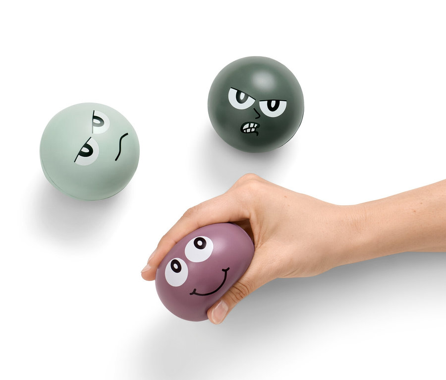 Eine Hand hält einen lila Anti-Stressball, im Hintergrund sind zwei weitere Anti-Stressbälle.