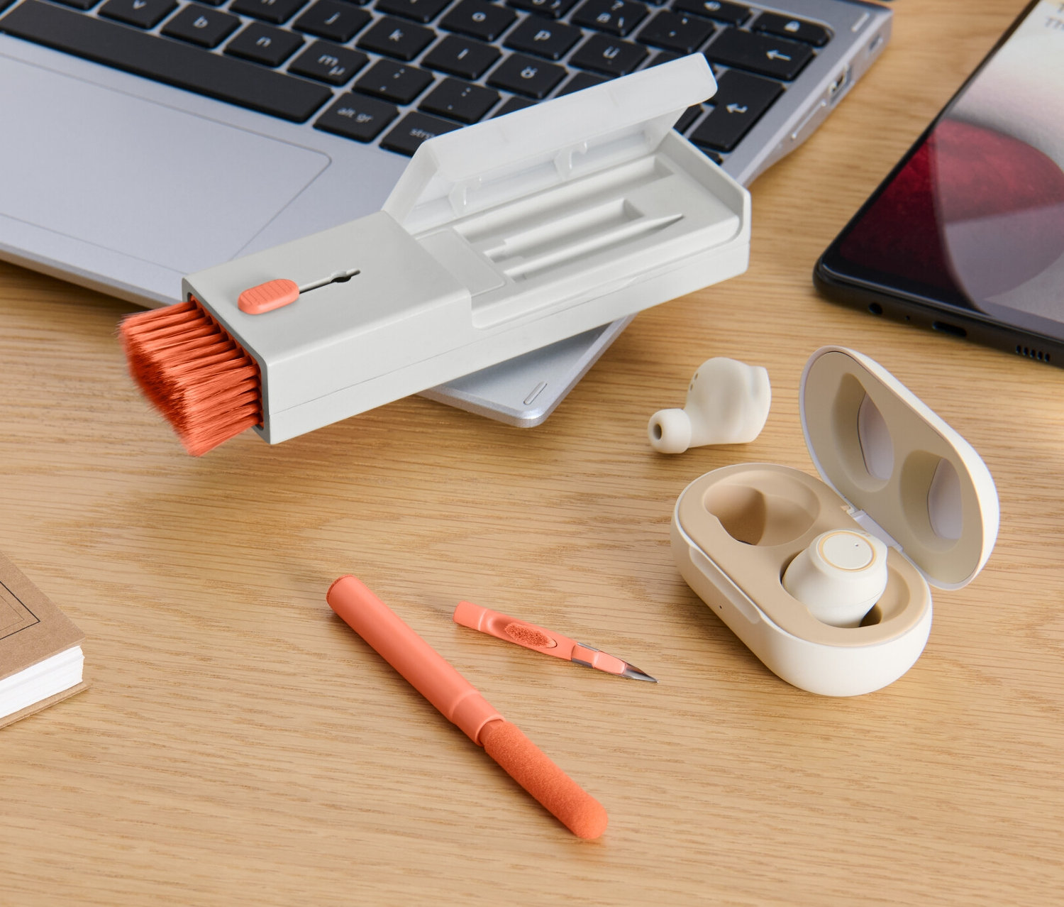 Auf einem Schreibtisch liegen ein Laptop, ein Telefon, Kopfhörer in einem Etui, ein Stift, ein Notizbuch und ein 4-in-1-Schreibtisch-Reinigungs-Set.