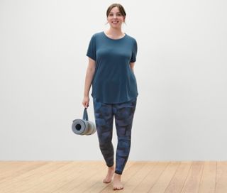 Frau trägt ein Longshirt in Navy und eine Wende-Sporttight in Schwarz/Navy und hält eine zusammengerollte Yoga-Matte.