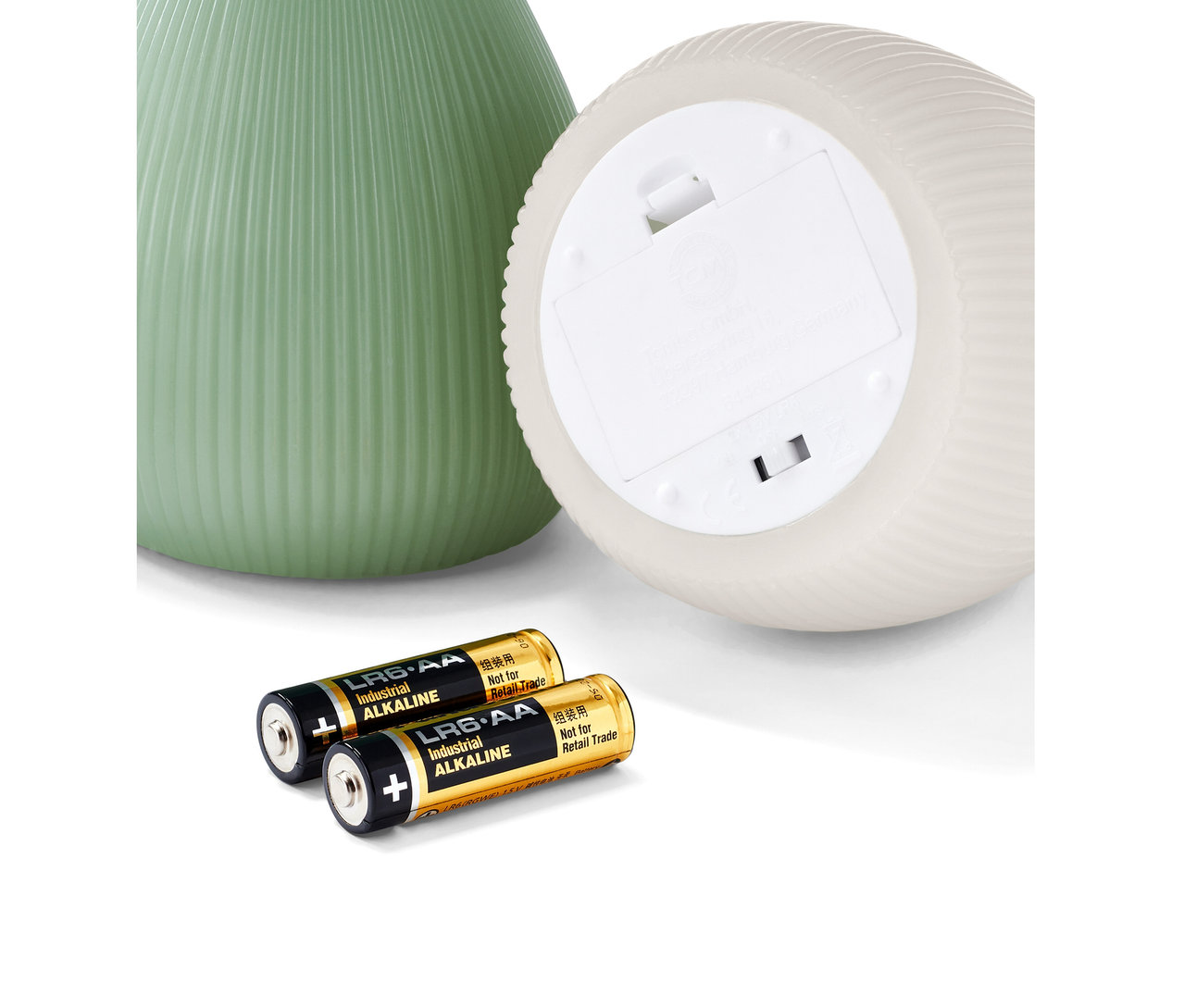 Zwei LED-Echtwachskerzen, eine grüne und eine weiße, liegen neben zwei Batterien.