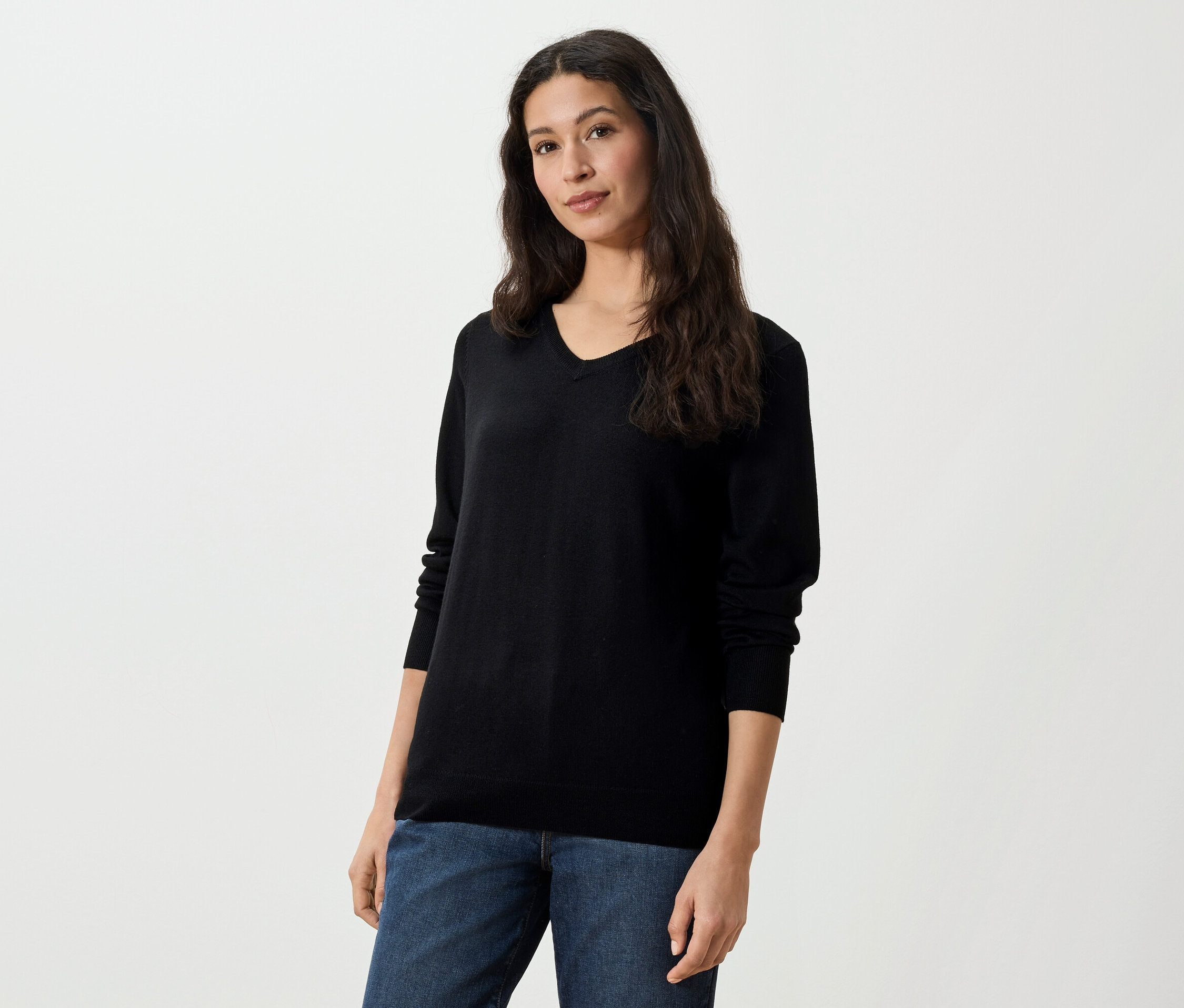 Frau mit langen dunklen Haaren trägt einen schwarzen Pullover mit V-Ausschnitt und Jeans.