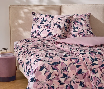Blumige Bettwäsche mit Kissen auf einem Bett mit Kopfteil und Nachttisch.