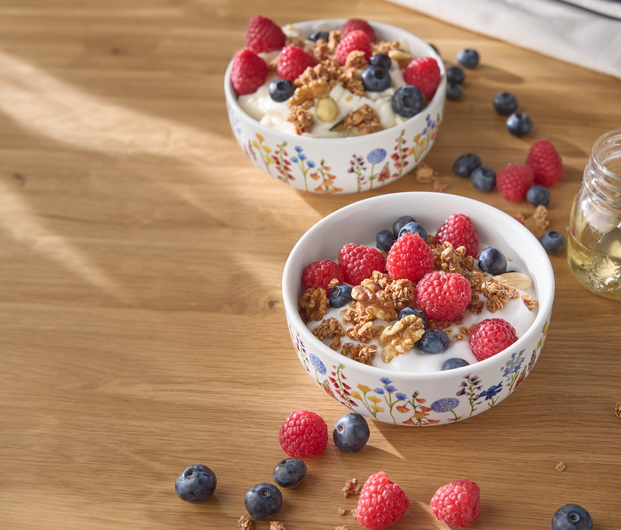 Zwei Schalen Joghurt mit Himbeeren, Blaubeeren und Nüssen auf einem Holztisch.