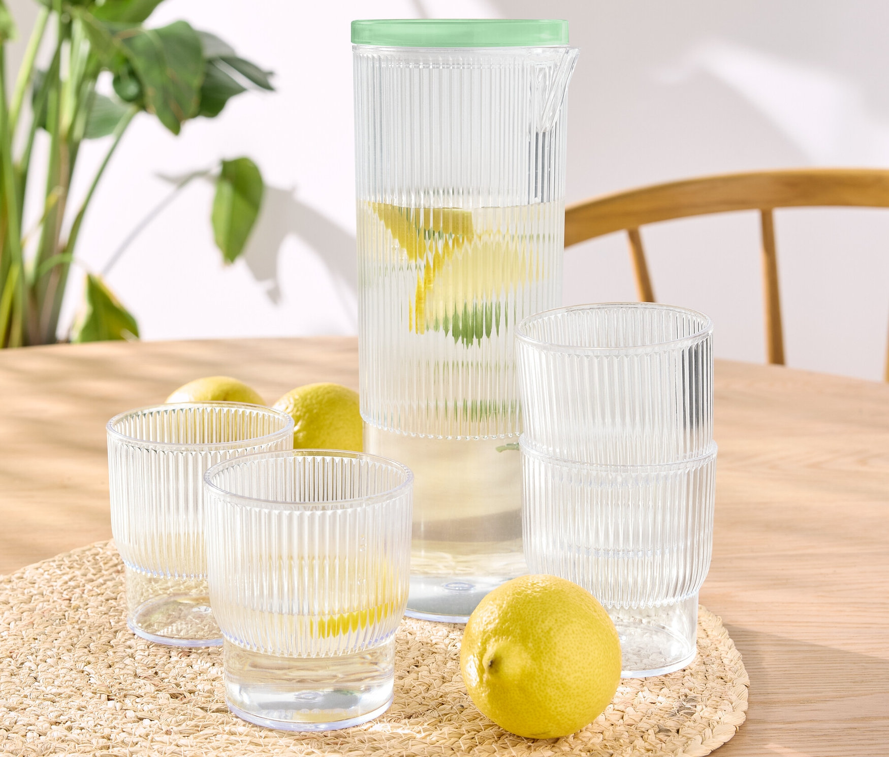 Auf einem Tisch stehen vier Kunststoff-Trinkbecher mit Krug, einige mit Wasser und Zitrone gefüllt.