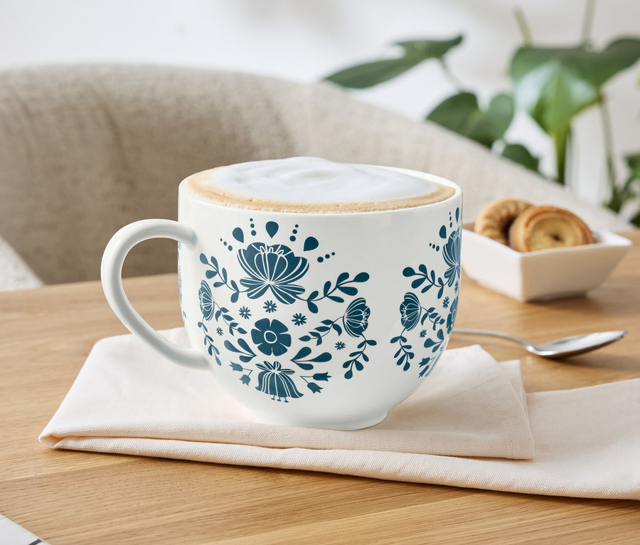 Eine Tasse Kaffee mit blauem Blumenmuster auf einer Serviette.