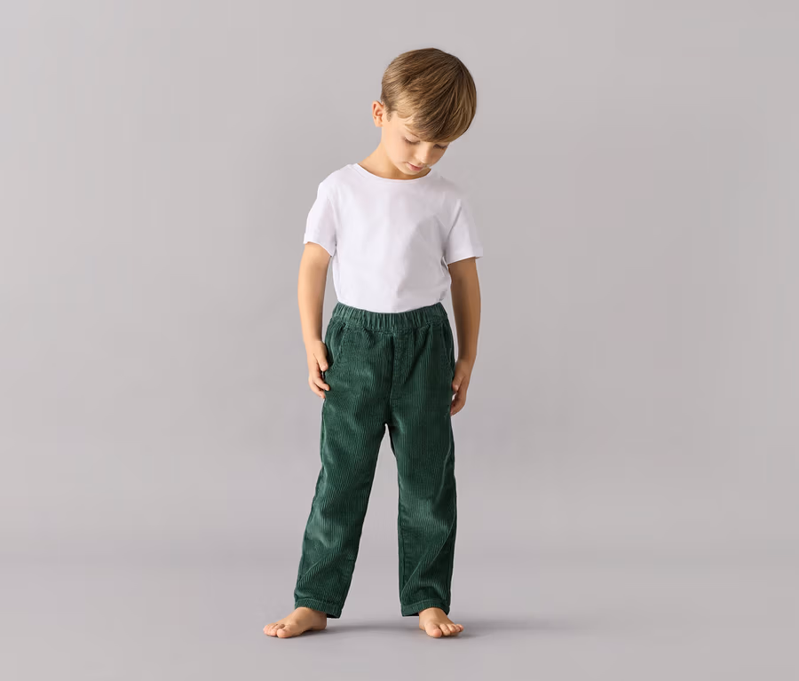 Junge steht und trägt eine grüne Kinder-Pull on pants – Fit »Mika« und ein weißes T-Shirt.
