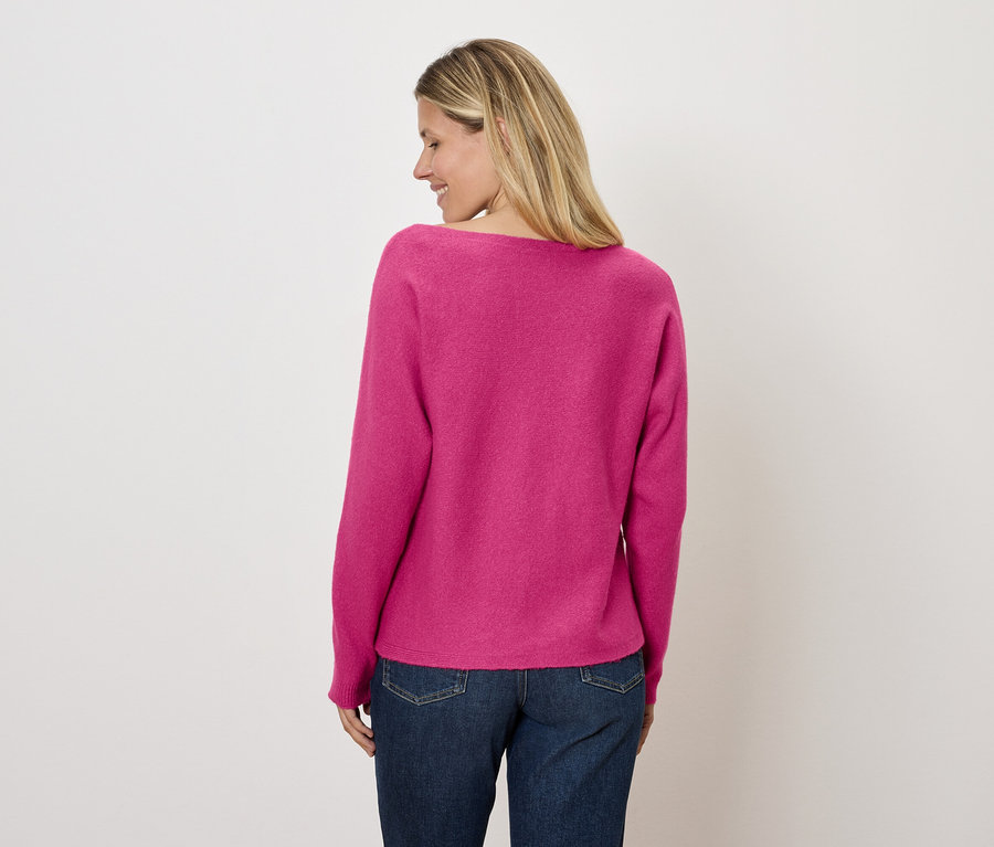 Frau blickt nach links und trägt einen pinken Pullover und Jeans.