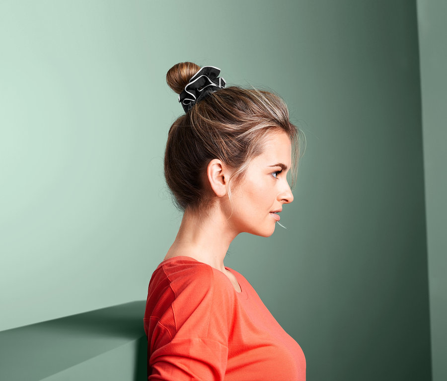 Profil einer Frau mit Duttfrisur, die 2 Sport-Haarbänder hält, schwarz und weiß.