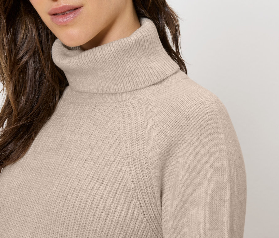 Detailaufnahme einer Frau, die einen beigen Rollkragenpullover trägt.