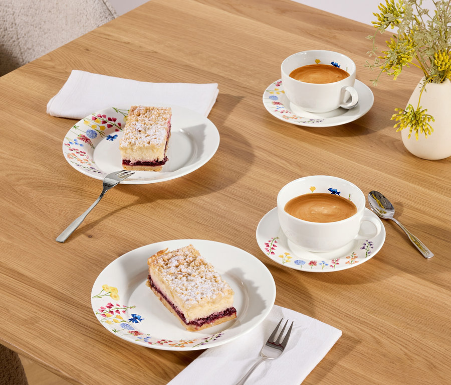 Zwei Stücke Kuchen und zwei Tassen Kaffee auf einem Holztisch.