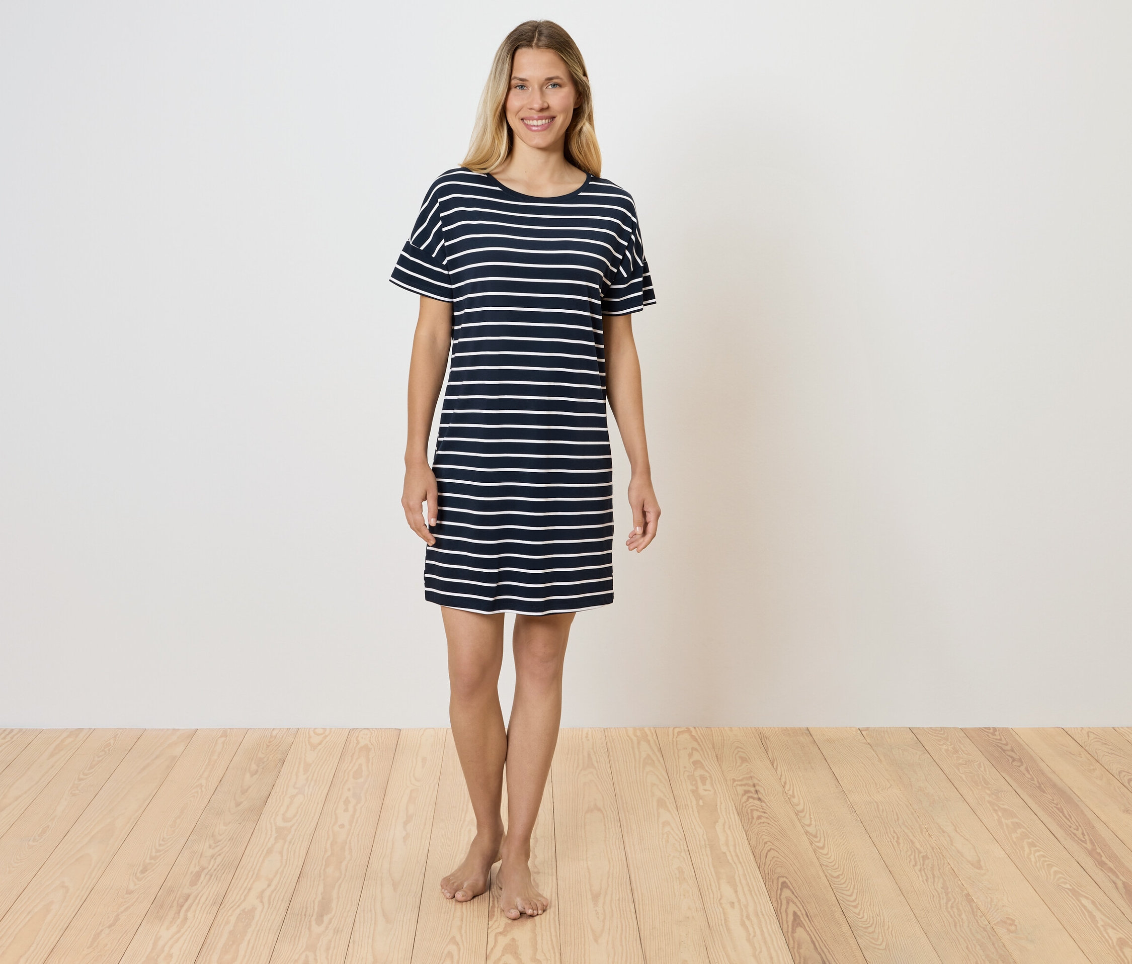 Eine Frau steht auf einem Holzboden und trägt ein gestreiftes T-Shirt-Kleid.