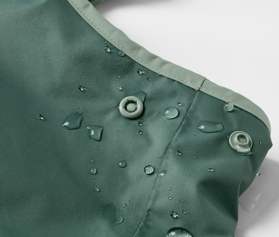 Detailaufnahme einer grünen Kinder-Thermo-Regenhose mit Wassertropfen und Druckknöpfen.