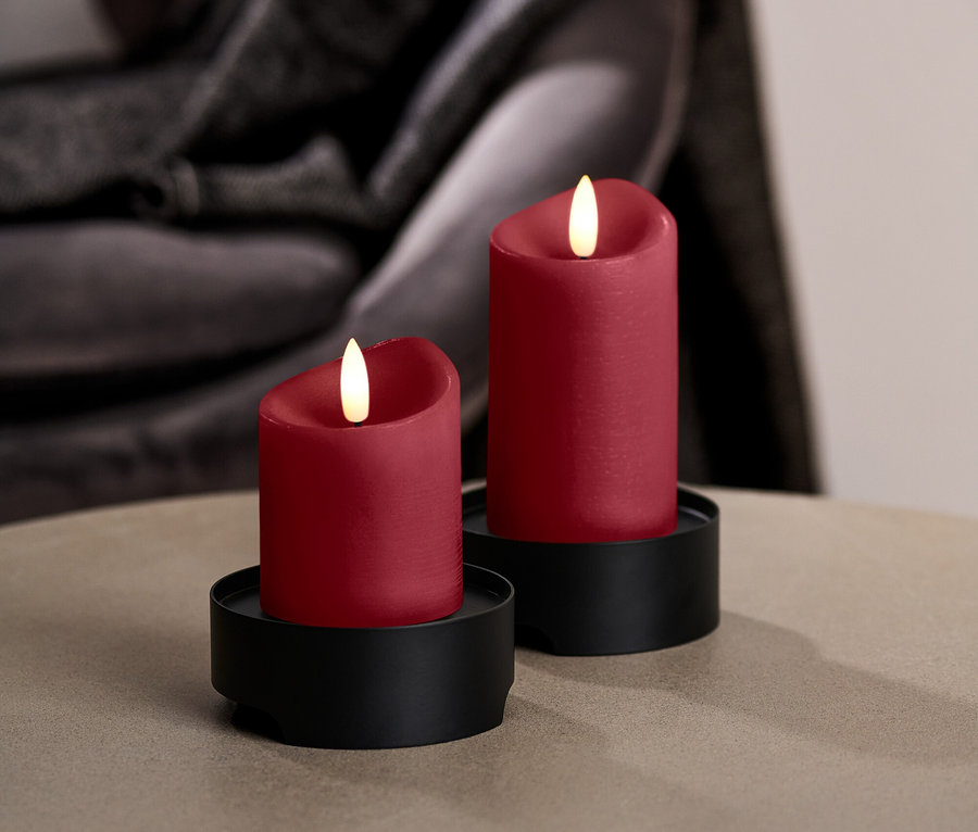 Zwei rote LED-Kerzen auf schwarzen Ständern stehen auf einem runden Tisch.