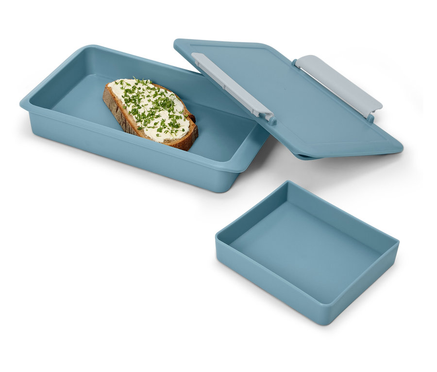 Ein belegtes Brot mit Kräutern in einer blauen Lunchbox mit Deckel und eine leere blaue Schale.