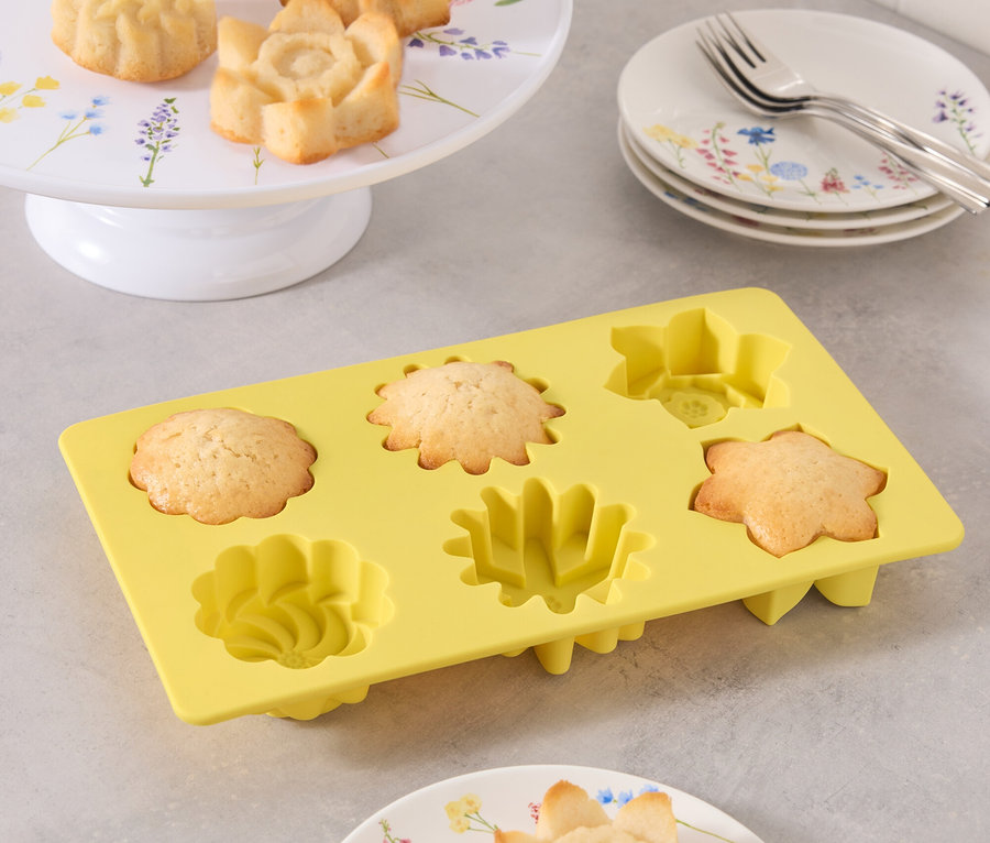 Blumenförmige Kuchenförmchen auf Tellern und in gelber Silikonform.
