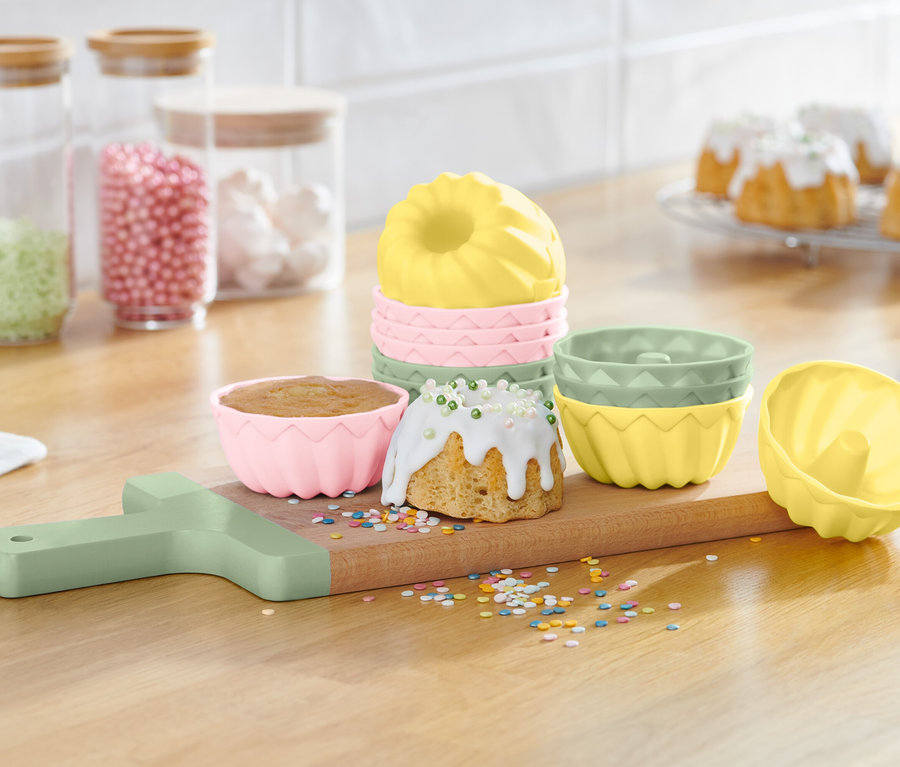 Gugelhupfformen auf einem Holzbrett mit fertigen Gugelhupfen und Streuseln.