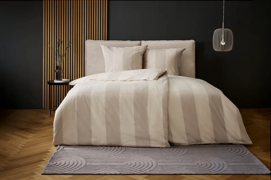 Schlafzimmer mit Bettwäsche mit beigen Streifen und grauem Teppich mit Kreismuster.