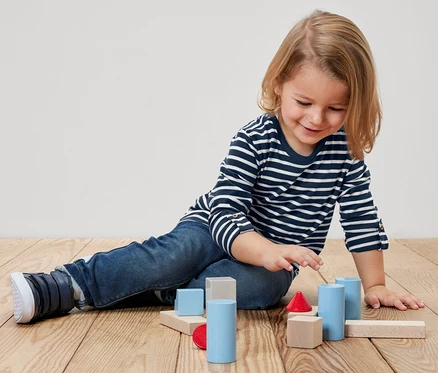 Kind sitzt am Boden und spielt mit bunten Holzklötzen. Es trägt ein 2 Kinder-Langarmshirts.