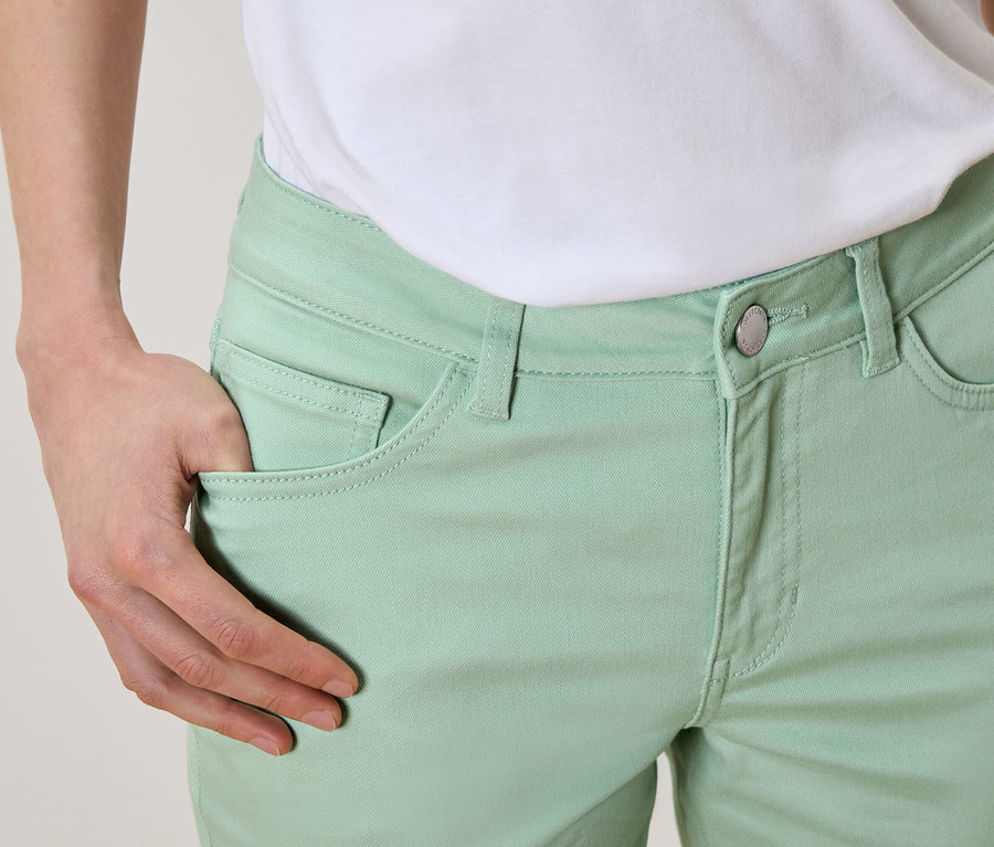 Nahaufnahme einer Person mit einer Hand in der Tasche einer hellgrünen Hose, dazu ein weißes T-Shirt.