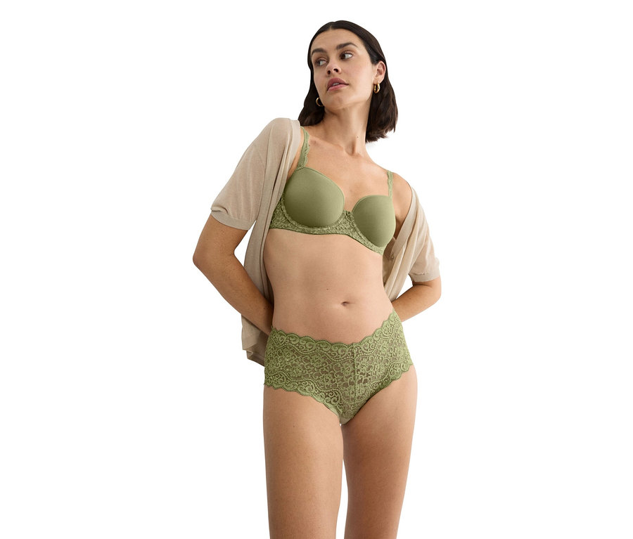 Frau trägt grünen BH mit Spitzenbesatz und passende Spitzenslips, dazu eine beige Strickjacke.