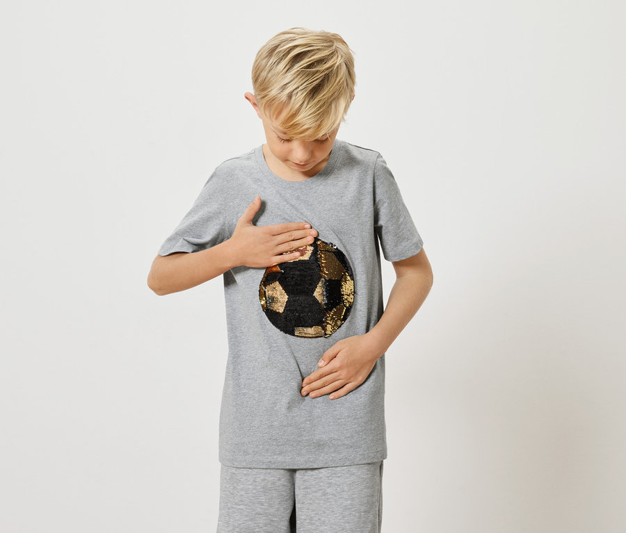 Ein blonder Junge in einem grauen T-Shirt mit einem Fußballmotiv berührt das Motiv.