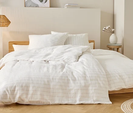 Bett mit weißer Bettwäsche mit dünnen Streifen, Nachttisch mit Vase und Lampe hängen von der Decke.