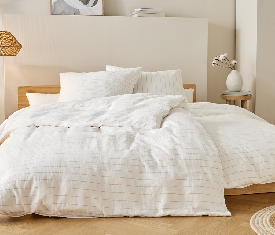 Bett mit weißer Bettwäsche mit dünnen Streifen, Nachttisch mit Vase und Lampe hängen von der Decke.