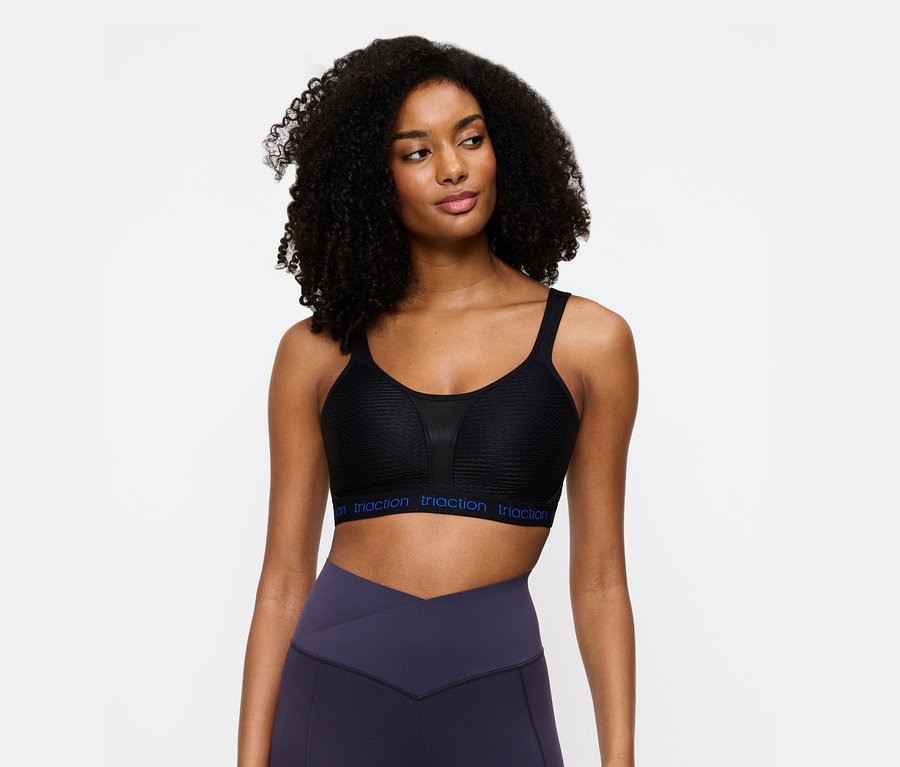 Frau trägt einen schwarzen Triaction Sport-BH und violette Leggings.