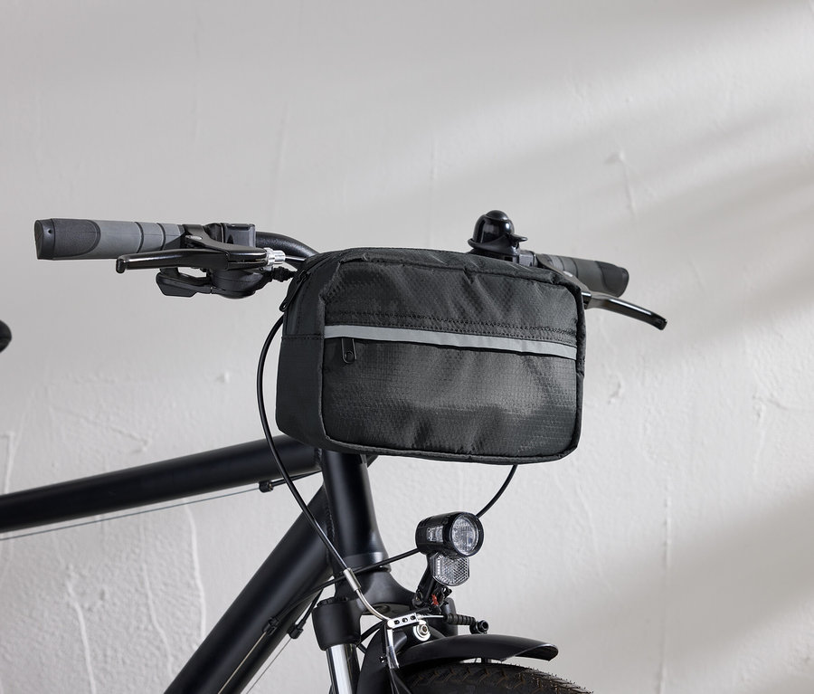 Detailansicht eines schwarzen Fahrrads mit einer schwarzen Lenkertasche und einem Fahrradlicht vor einer weißen Wand.