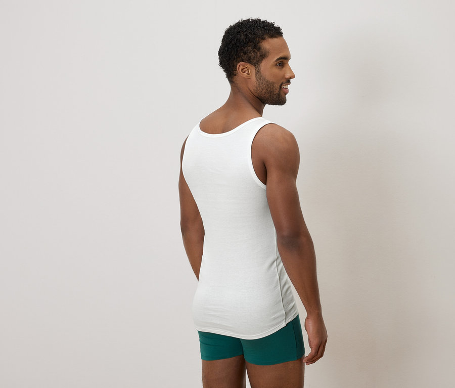Mann von hinten gesehen, der ein weißes Unterhemd und grüne Boxershorts trägt und zur Seite schaut.