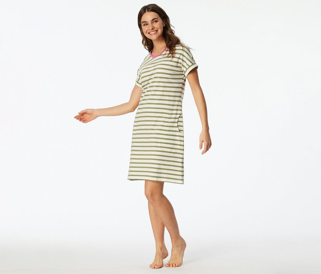 Lächelnde Frau in einem kurzärmeligen, knielangen SCHIESSER Nachthemd mit olivgrünen und beigefarbenen Streifen, rosa Kragen und Tasche, barfuß stehend.