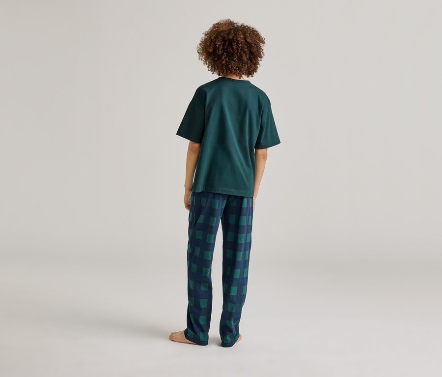 Junge mit lockigem Haar, von hinten gesehen, trägt ein grünes T-Shirt und eine blau-grün karierte Hose.