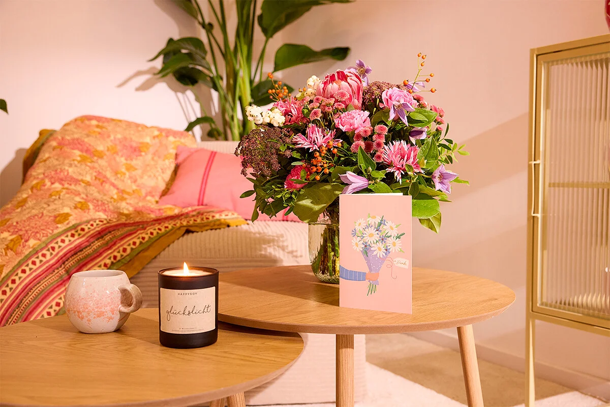 Auf einem Couchtisch stehen eine Blumenvase, eine Kerze und eine Grußkarte.