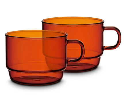 Zwei orangefarbene Glasbecher mit Henkel stehen nebeneinander.