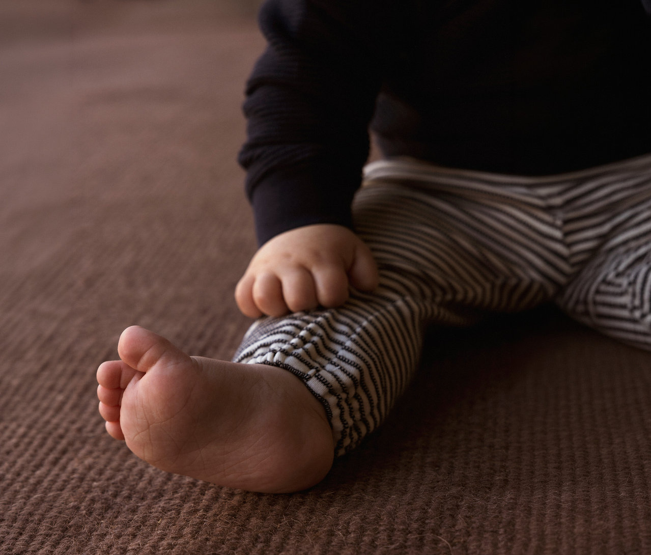 Nahaufnahme eines Babys in einer schwarzen Strickjacke und einer NAME IT Baby-Jerseyhose mit Streifen.