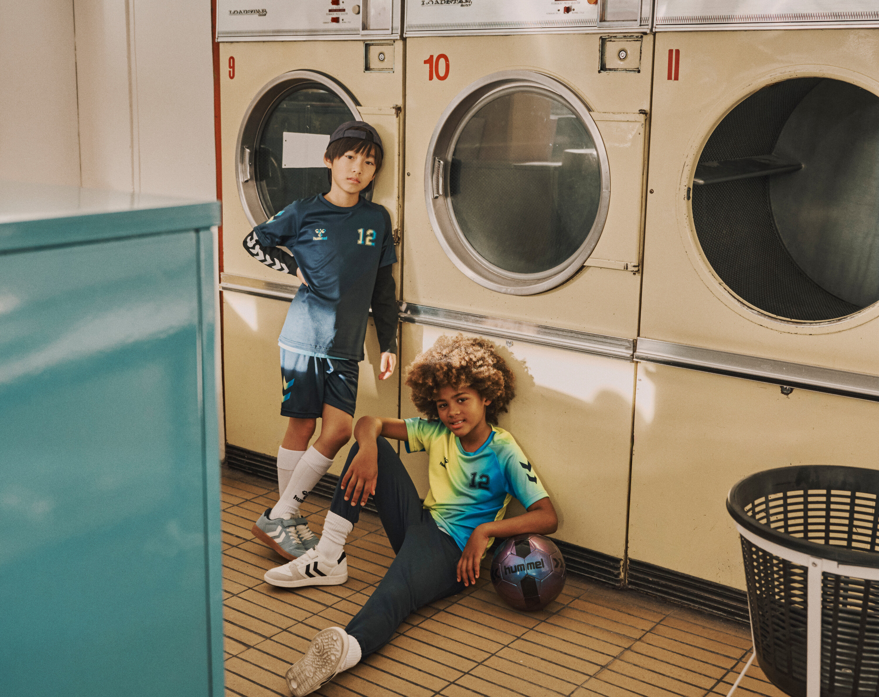 Zwei Jungen posieren in einem Waschsalon, einer steht und einer sitzt mit einem Fußball.