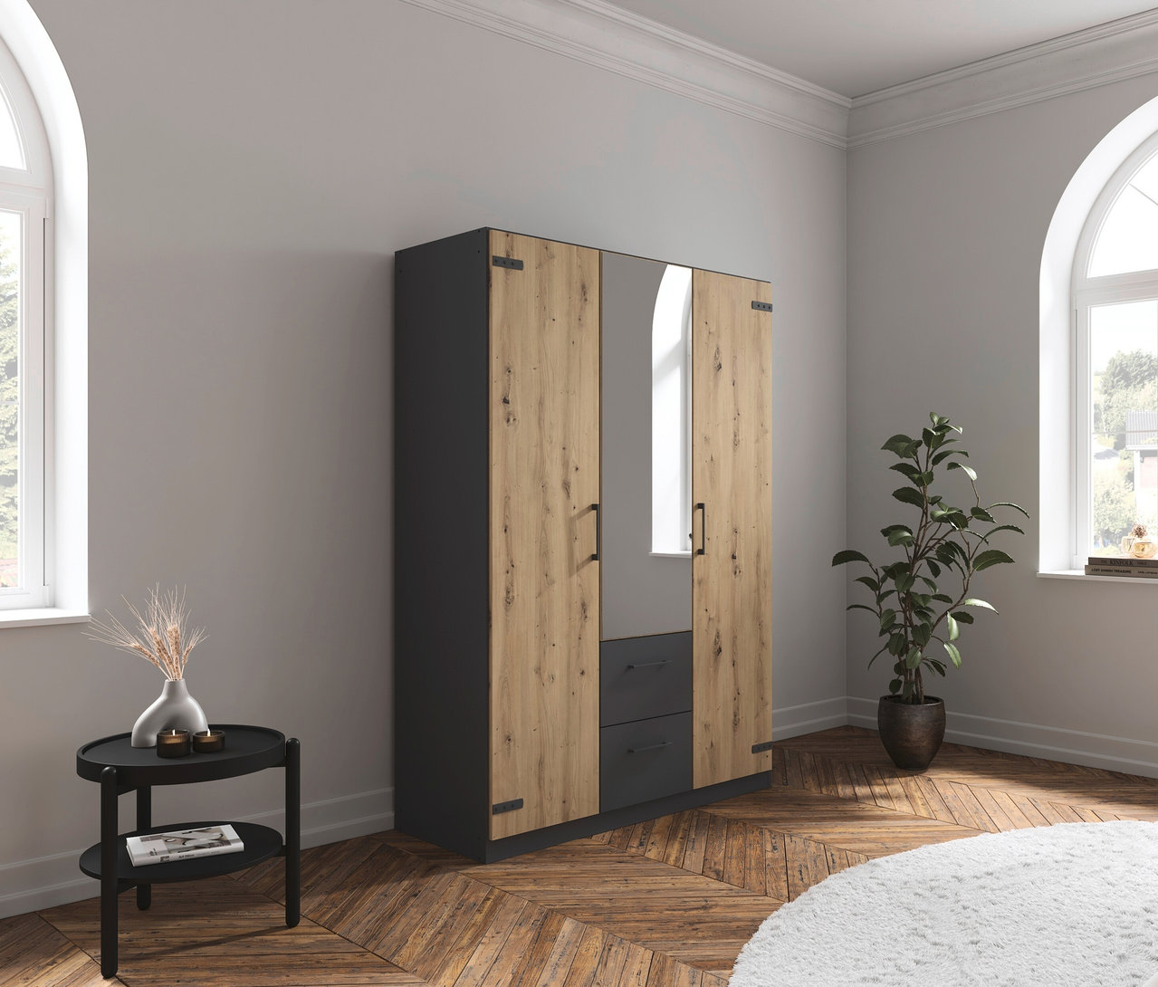 Im Zimmer steht ein rauch Drehtürenschrank »Butte« mit 3 Türen, neben einem schwarzen Tischchen und einer Zimmerpflanze.