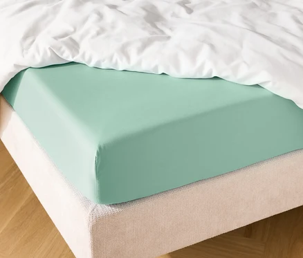 Bett mit mintgrünem Spannbettlaken und weißer Bettdecke.