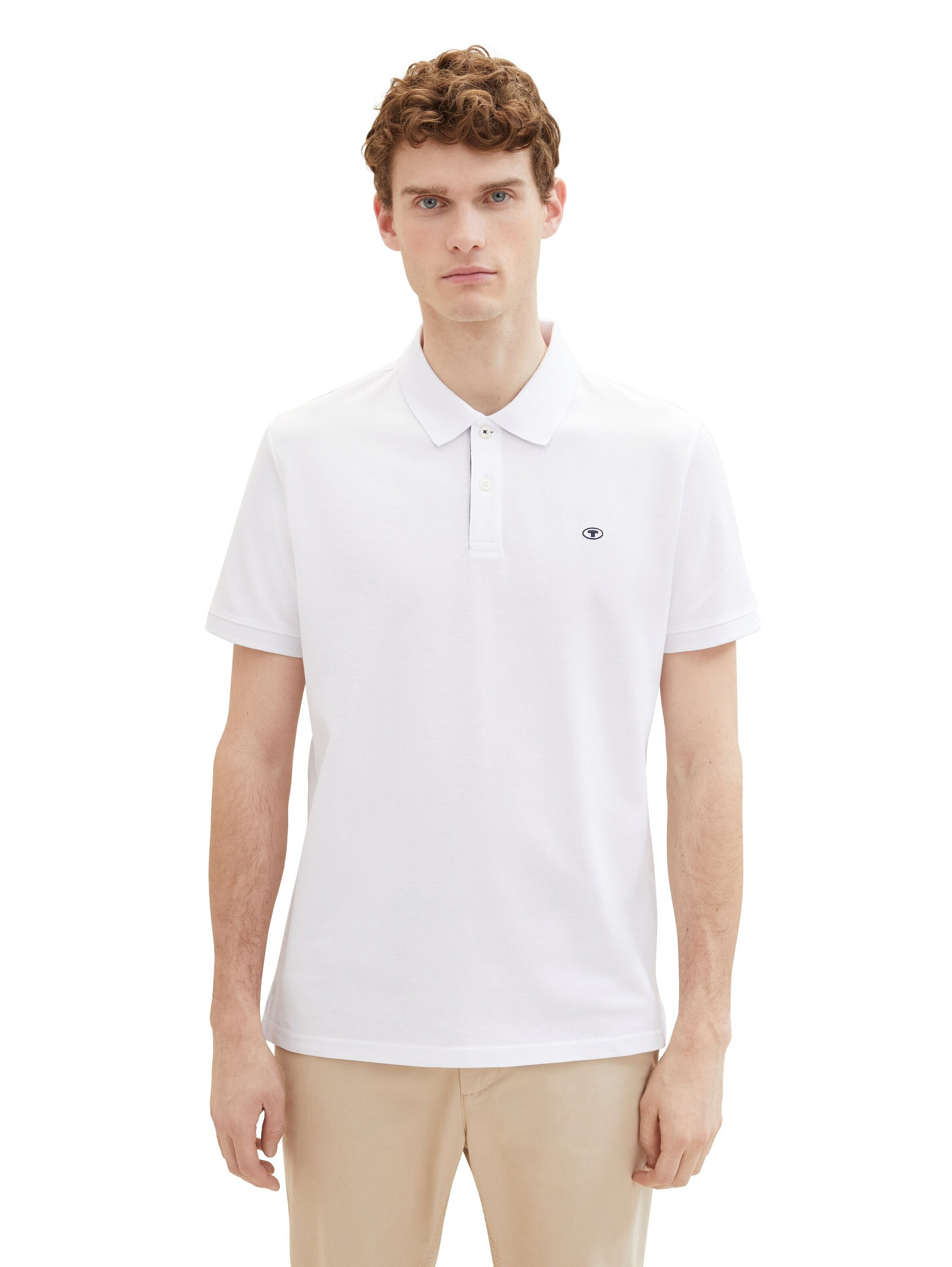 Mann mit lockigem Haar trägt ein weißes Poloshirt und eine beige Hose.