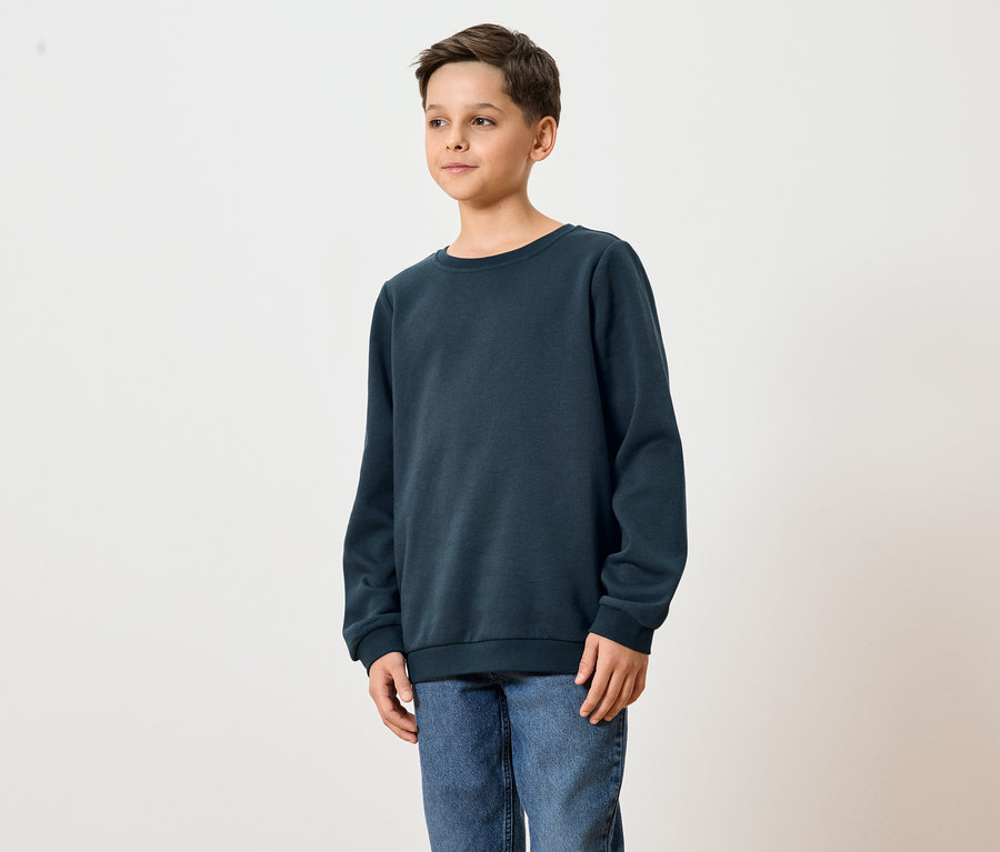 Ein junger Mann trägt ein dunkelblaues Sweatshirt und Jeans.