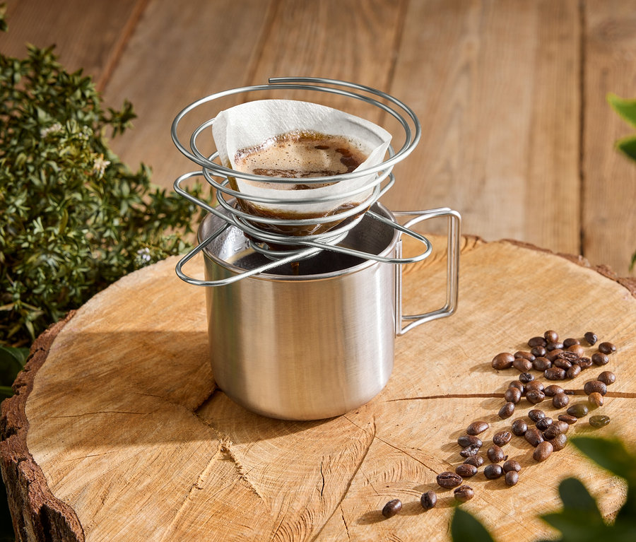 Kaffee wird mit einem spiralförmigen Kaffeefilterhalter in einen Edelstahlbecher auf einem Baumstumpf gegossen.