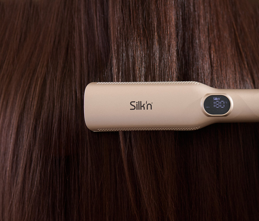 Nahaufnahme von einem Silk'n Glätteisen, das durch braunes Haar gleitet.