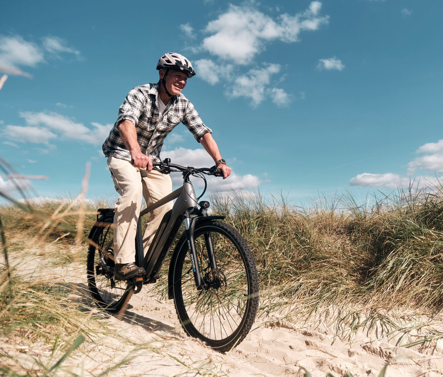 Mann fährt ein graues FISCHER Trekking-E-Bike TERRA 2.2 ACTIVE mit Diamant Rahmen auf sandigem Untergrund.