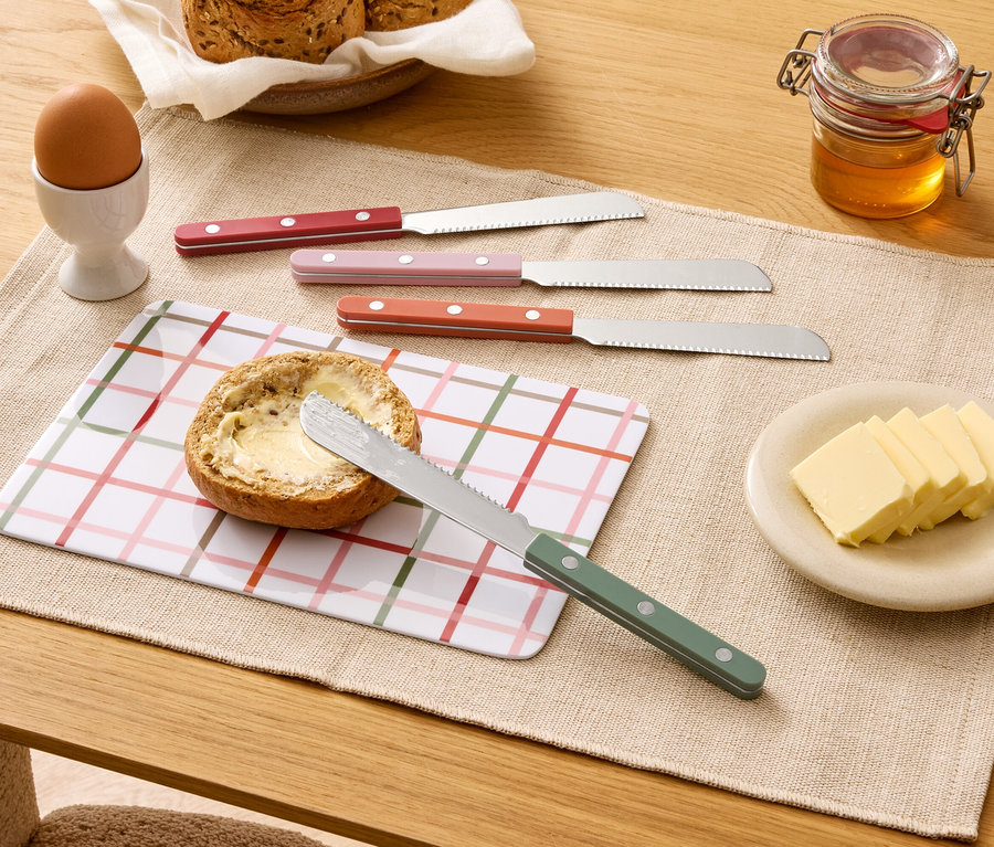 Auf einem Tisch liegen ein belegtes Brötchen, vier Messer, Butter, Honig, ein Ei und Brot.