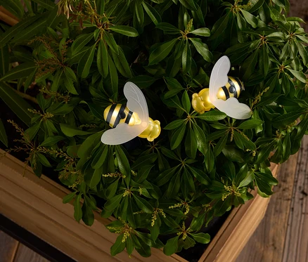 Zwei gelbe und schwarz gestreifte Bienen mit durchscheinenden Flügeln inmitten von grünen Blättern in einem Holzkasten.