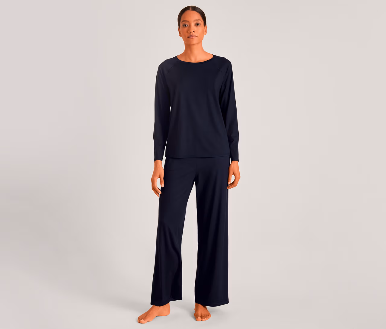 Frau in dunkelblauem Langarmshirt und passender weiter Hose, barfuß stehend.
