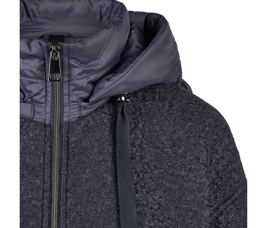 Nahaufnahme einer dunkelblauen Jacke mit strukturiertem, lockigem Hauptteil und einer glatten, wattierten Kapuze. Ein silberner Reißverschluss verläuft vorne, und ein dunkelblauer Kordelzug ist am Kragen sichtbar.